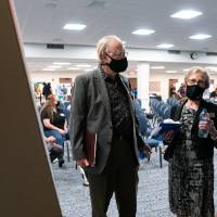 Scholar wearing mask presenting poster to two guests wearing masks.
